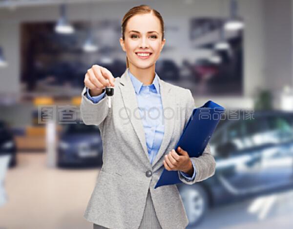 汽车业务,汽车销售,手势和人的概念-快乐的女商人或售货员与文件夹给车钥匙在汽车展示背景